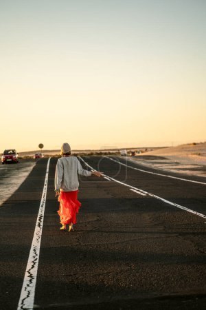 Téléchargez les photos : Photo d'une jeune voyageuse insouciante marchant sur la route, attendant l'auto-stop. Concept de voyage. La soif d'errance. Des rêves. Tourisme. - en image libre de droit