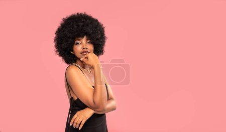Foto de Elegante joven con peinado afro y maquillaje glamour posando sobre fondo de estudio rosa pastel. Un montón de espacio de copia. - Imagen libre de derechos