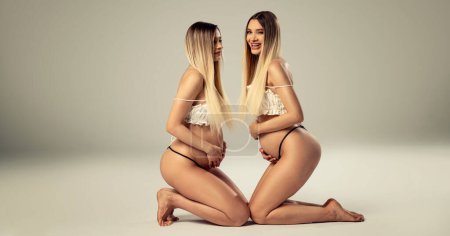 Téléchargez les photos : Photo conceptuelle de deux belles jumelles enceintes posant ensemble en studio. Beaucoup d'espace pour copier. Les mères. La famille. Une nouvelle vie. - en image libre de droit