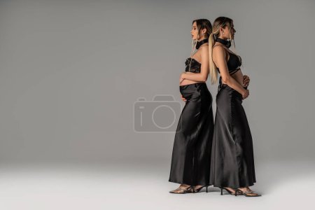 Téléchargez les photos : Deux femmes enceintes à la mode portant des vêtements élégants, posant ensemble en studio. Sœur jumelle. Beaucoup d'espace de copie pour votre texte - en image libre de droit