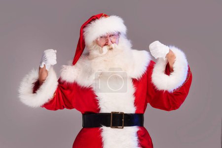 Téléchargez les photos : Le vrai vieux Père Noël en montrant son pouvoir, posant sur un fond de studio gris. Joyeux Noël et bonne année ! Espace de copie. Vente de Noël, concept de réduction. - en image libre de droit