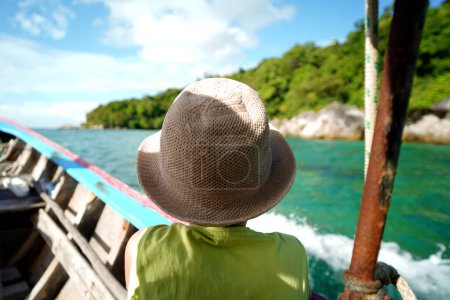 Photo for Back view of a boy in summer hat sitting in the wooden boat. Travel. Tourism. Thailand. Asia. Tropical destination. - Royalty Free Image
