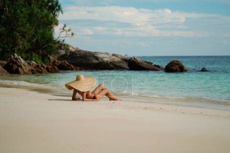 Téléchargez les photos : Des vacances. L'été. Femme relaxante sur la plage tropicale sablonneuse portant un grand chapeau, bronzant. Voyage. Touristique. Thiland. Asie. - en image libre de droit