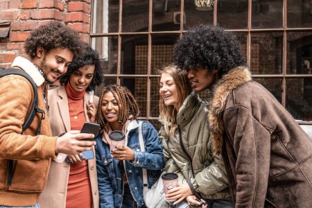 Foto de Grupo de jóvenes amigos multiétnicos hablando y viendo las redes sociales en el teléfono móvil. Estilo de vida multirracial de moda. Foto al aire libre. - Imagen libre de derechos