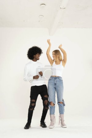 Foto de Feliz pareja interracial bailando juntos en el estudio, sonriendo, mirando los unos a los otros. Emociones de personas reales. Amor, amistad, hobby. - Imagen libre de derechos