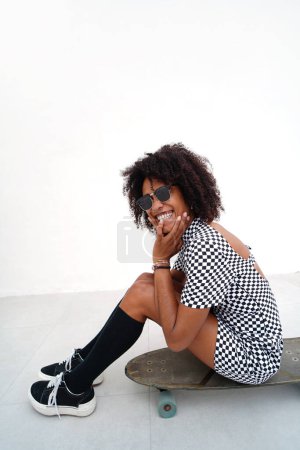 Photo for Happy girl with beautiful smile in trendy street style clothes enjoying riding skateboard at sunny day. Real people lifestyle. Hobby. Happiness - Royalty Free Image