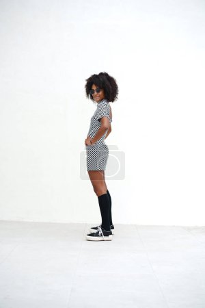 Foto de Mujer joven con peinado afro de pie y posando en la pared blanca. Chica vestida con ropa casual de moda, estilo callejero. Un montón de espacio de copia - Imagen libre de derechos