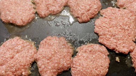 Photo for Raw hamburger patties frying on a stove top griddle hot grease and surface food background - Royalty Free Image