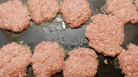 Photo for Raw hamburger patties frying on a stove top griddle hot grease and surface food cooking - Royalty Free Image