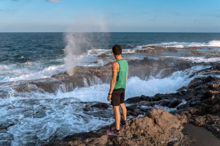 young man stands after exercising in front of a rock formation in the sea