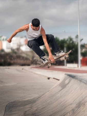 Foto de Un joven con una camiseta blanca haciendo un truco llamado deshuesado en una rampa de un parque de skate. composición vertical - Imagen libre de derechos