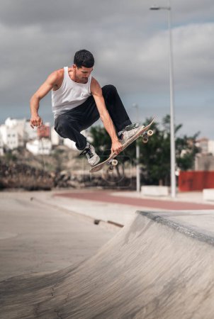 junger Mann mit weißem T-Shirt, der in einer Rampe eines Skateparks einen Trick namens knochenlos macht. vertikale Zusammensetzung