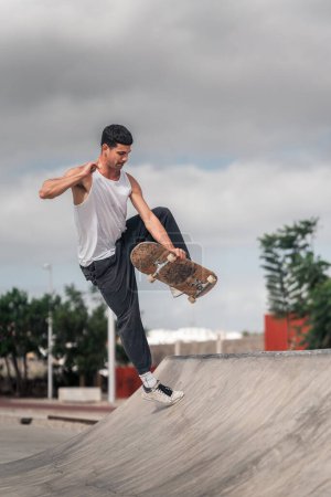 young man with white t-shirt doing a trick called boneless in a ramp of a skate park. vertical composition