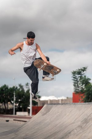 Foto de Un joven con una camiseta blanca haciendo un truco llamado deshuesado en una rampa de un parque de skate. composición vertical - Imagen libre de derechos