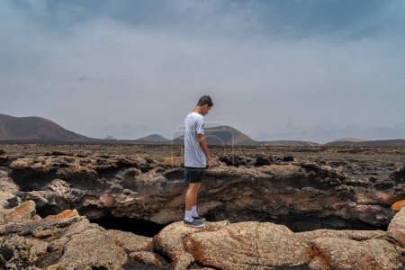 Young man looks out at the entrance to Las Palomas Cave. Timanfaya National Park. Lanzarote. Canary Islands