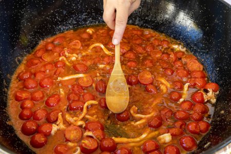 Photo for Cooking Italian stew with seafood and tomatoes in a big frying pan. Mediterranean Apulian traditional food with fresh stewed clams, shrimps, mussels, octopus and squid - Royalty Free Image