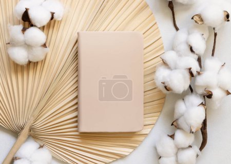 Blank hardcover textbook on dried palm leaf with cotton flowers top view. Textbook cover mockup, planner with place fot text. Educational, business and organizing concept