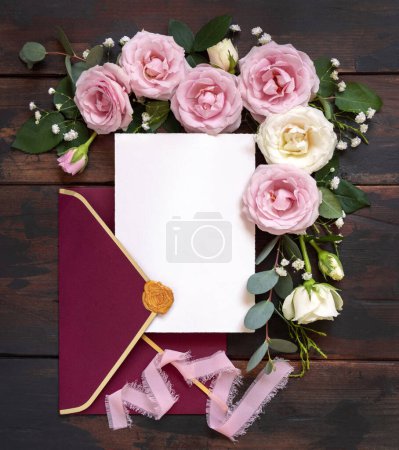 Photo for Card and red envelope between pink and cream roses on brown wood top view,  wedding mockup. Romantic scene with cards, envelope and pastel flowers flat lay. Valentines, Spring or Mothers day concept - Royalty Free Image