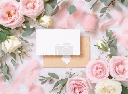 Photo for Blank card and envelope between light pink roses and silk ribbons on marble top view,  wedding mockup. Romantic scene with horizontal card and pastel flowers flat lay. Valentines, Spring or Mothers day - Royalty Free Image