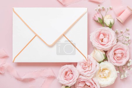 Foto de Envelope  between light pink roses and silk ribbons on pink top view,  wedding mockup. Romantic scene with blank envelope and pastel flowers flat lay. Valentines, Spring or Mothers day concept - Imagen libre de derechos