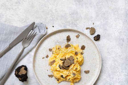 Photo for Scrambled eggs with sliced fresh black truffles from Italy served in a plate near fork and knife top view. Italian cousine, gourmet breakfast - Royalty Free Image