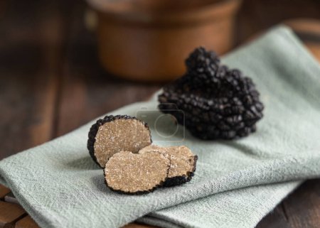 Foto de Whole and sliced black truffles mushroom on wooden board on green napkin on dark brown table, close up. Culinary delight ingredient. - Imagen libre de derechos
