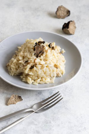 Foto de Risotto with wild porcini mushrooms and black truffles from Italy served in a plate close up on white table, negative space. Eating Italian gourmet cousine - Imagen libre de derechos