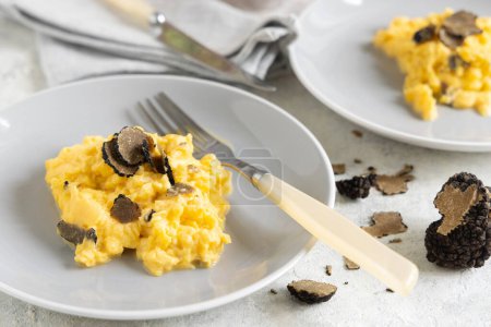 Photo for Scrambled eggs with sliced fresh black truffles from Italy served in a plate near fork and knife close up. Italian cousine, gourmet breakfast - Royalty Free Image