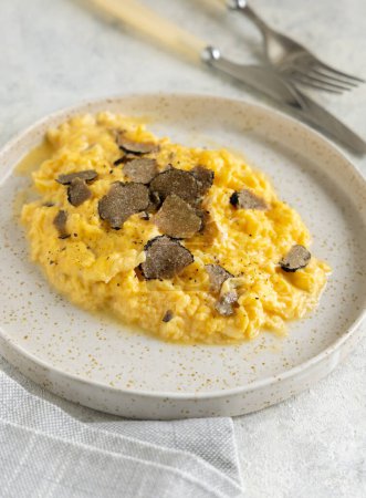 Photo for Scrambled eggs with sliced fresh black truffles from Italy served in a plate near fork and knife close up. Italian cousine, gourmet breakfast - Royalty Free Image