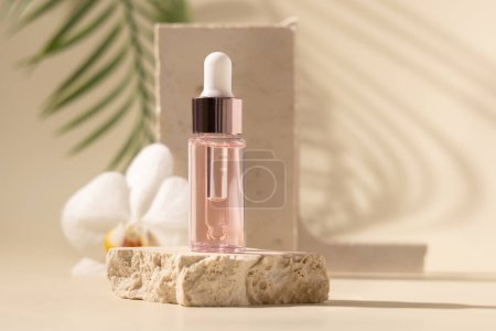 Dropper Bottle on stone near white orchid flowers with palm leaf on beige, close up. Skincare beauty product, essential oil or serum. Exotic cosmetics, pastel minimal compositio
