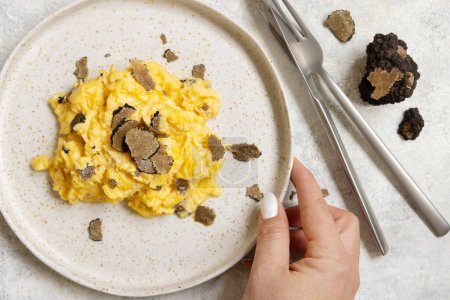 Photo for Hand with plate with Scrambled eggs with fresh black truffles top view. Italian cousine, gourmet breakfast - Royalty Free Image