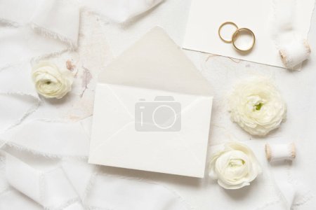 Photo for Blank envelope near cream roses, white silk ribbons and wedding rings top view,  wedding mockup. Romantic scene with  pastel flowers flat lay. Valentines, Spring or Mothers day concept - Royalty Free Image
