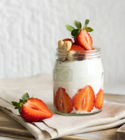 Photo for Greek yogurt, nuts and strawberries in a glass jar on a wooden tray with a napkinn, close up. Healthy breakfast with fruits and nuts. Great way to eat protein - Royalty Free Image