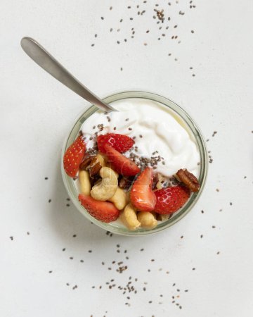 Foto de Yogur griego, nueces y fresas en un frasco de vidrio con una cuchara en una mesa blanca vista superior. Desayuno saludable con frutas y frutos secos. Gran manera de comer proteínas - Imagen libre de derechos