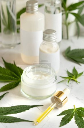 Photo for Blank Cream jar and bottles near green cannabis sativa leaves on a marble table. Cosmetic Mockup, Copy space. Organic skincare beauty product. Eco friendly body or hand cream with hem - Royalty Free Image