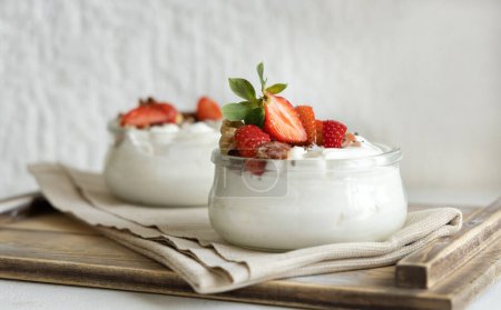 Photo for Greek yogurt, nuts and strawberries in a glass jars on a white table close up, copy space. Healthy breakfast with berries and nuts. Great way to eat protein - Royalty Free Image