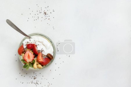 Foto de Yogur griego, nueces y fresas en un frasco de vidrio con una cuchara en una mesa blanca vista superior. Desayuno saludable con frutas y frutos secos. Gran manera de comer proteínas - Imagen libre de derechos