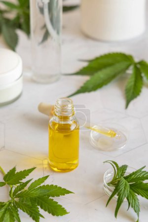 Photo for Opened Dropper bottle with pipette near green cannabis sativa leaves on a marble table close up. Organic skincare beauty product. Eco friendly CBD oi - Royalty Free Image