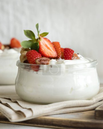 Téléchargez les photos : Yogourt grec, noix et fraises dans un bocal en verre sur une table blanche fermer. Petit déjeuner sain avec des baies et des noix. Excellente façon de manger des protéines - en image libre de droit