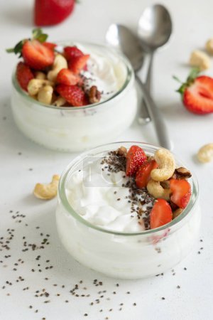 Téléchargez les photos : Pot en verre de yaourt grec, noix et fraises sur une table blanche, fermer, copier l'espace. Petit déjeuner sain avec des baies et des noix. Excellente façon de manger des protéines - en image libre de droit