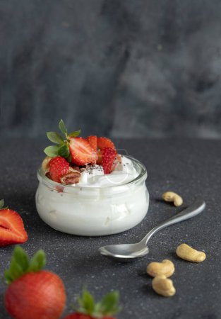 Photo for Glass jar of Greek yogurt, nuts and strawberries on grey concrete table with a spoon, close up, copy space. Healthy breakfast with fruits and nuts. Great way to eat protein - Royalty Free Image