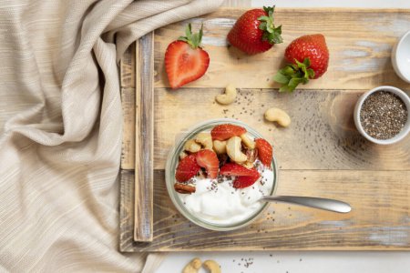 Photo for Glass jar of yogurt, nuts and strawberries on a wooden tray top view. Healthy breakfast with berries and nuts. Great way to eat protein - Royalty Free Image