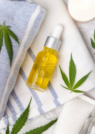 Photo for Dropper bottle with CBD oil near green cannabis leaves on bath towel top view. Organic healthcare product. Alternative medicine and cosmetic - Royalty Free Image