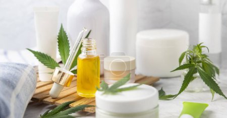 Dropper bottle with CBD oil and cream bottles green cannabis leaves close up in bathroom. Organic healthcare product. Alternative medicine for sleep and relax, CBD cosmetic