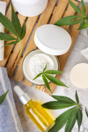 Téléchargez les photos : Pot à crème ouvert avec couvercle vierge et feuilles de cannabis vert sur plateau vue du dessus dans la salle de bain. Produits de beauté bio pour la peau, cosmétiques alternatifs CBD - en image libre de droit
