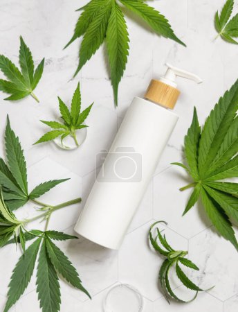 Téléchargez les photos : Blank White Une bouteille de pompe près de feuilles de cannabis sativa vertes sur une table en marbre vue sur le dessus. Maquette cosmétique, espace de copie. Produits de beauté bio pour la peau. Lotio CBD respectueux de l'environnement - en image libre de droit
