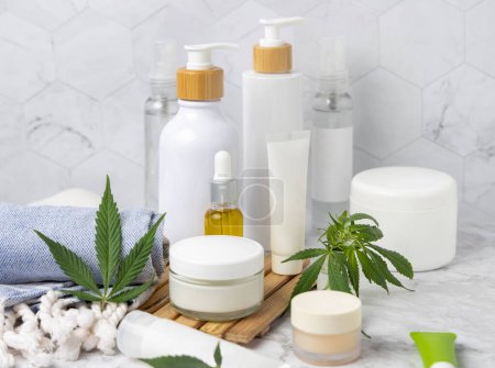 Photo for Blank cosmetic jars, tubes and bottles near green cannabis leaves on wooden tray in bathroom near other bottles, close up, mockup. Organic skincare beauty products, natural CBD cosmetic - Royalty Free Image