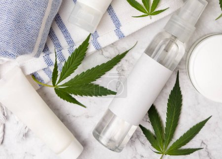 Photo for Spray bottle with blank label near green cannabis leaves on towel top view, mockup. Organic skincare beauty products, alternative CBD cosmetic - Royalty Free Image