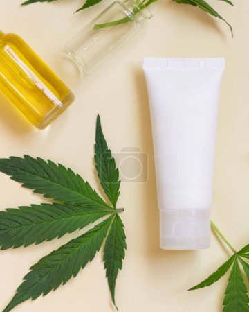 Téléchargez les photos : Tube à crème près de feuilles de cannabis vertes sur vue de dessus beige. Produits de beauté bio pour la peau, cosmétiques naturels alternatifs - en image libre de droit