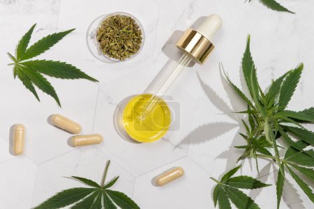 Photo for Bottle with CBD oil, Dry Tea infusion and capsules with hemp protein powder near green cannabis leaves top view on a marble table, hard shadows. Organic healthcare and skincare products - Royalty Free Image